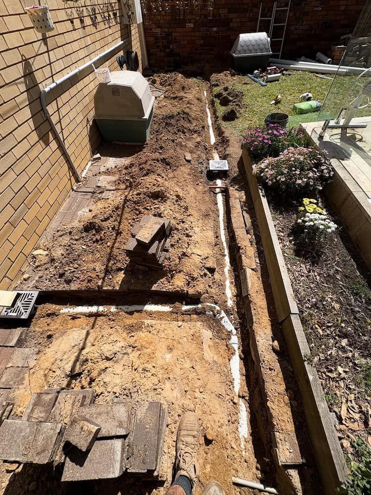 A Backyard Trench Showing Newly Installed White PVC Drainage Pipes — Crystal Clear Plumbing & Roofing in Wollongong, NSW