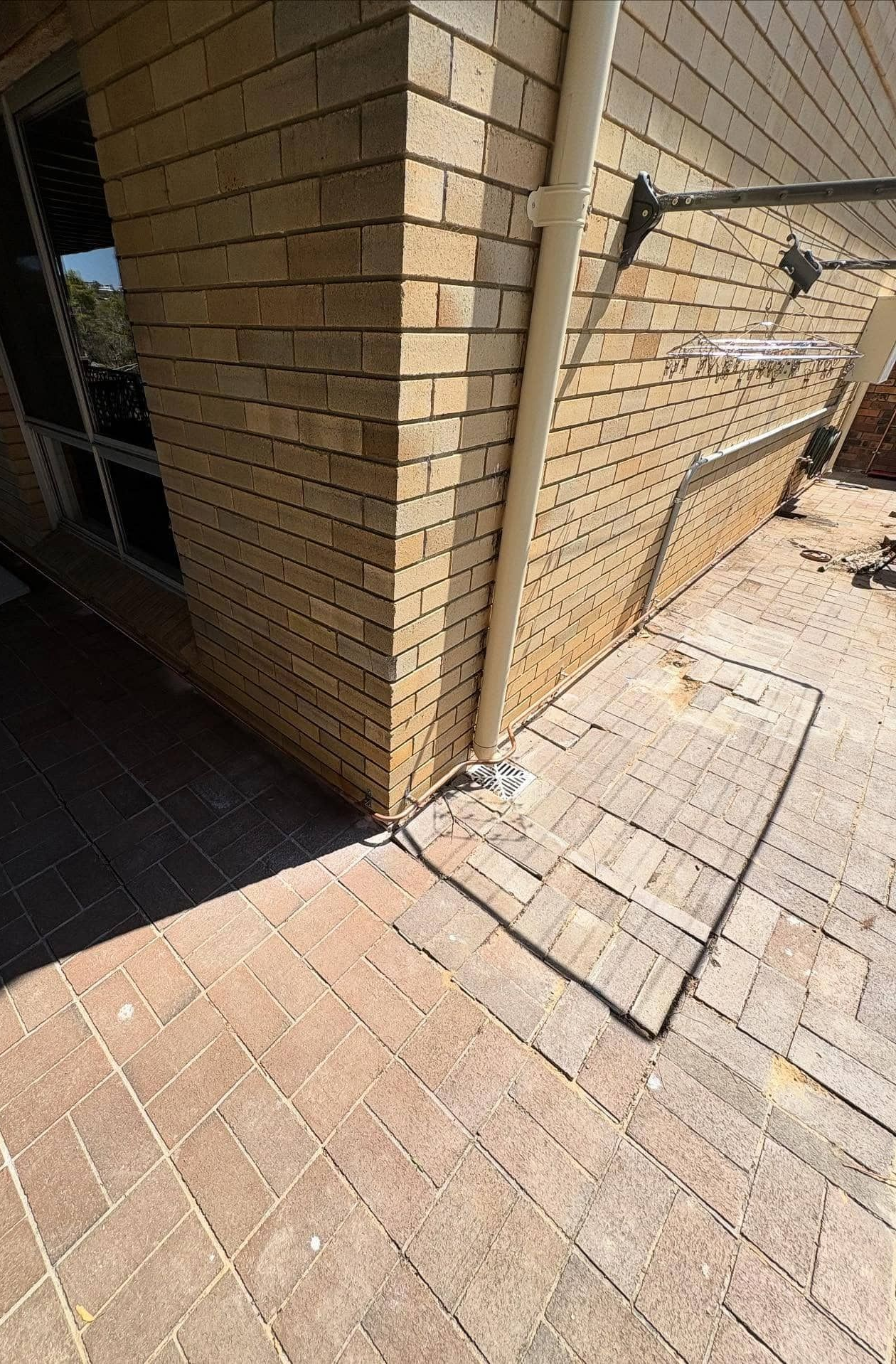 A Corner of a Tan Brick House With a Downpipe — Crystal Clear Plumbing & Roofing in Dapto, NSW
