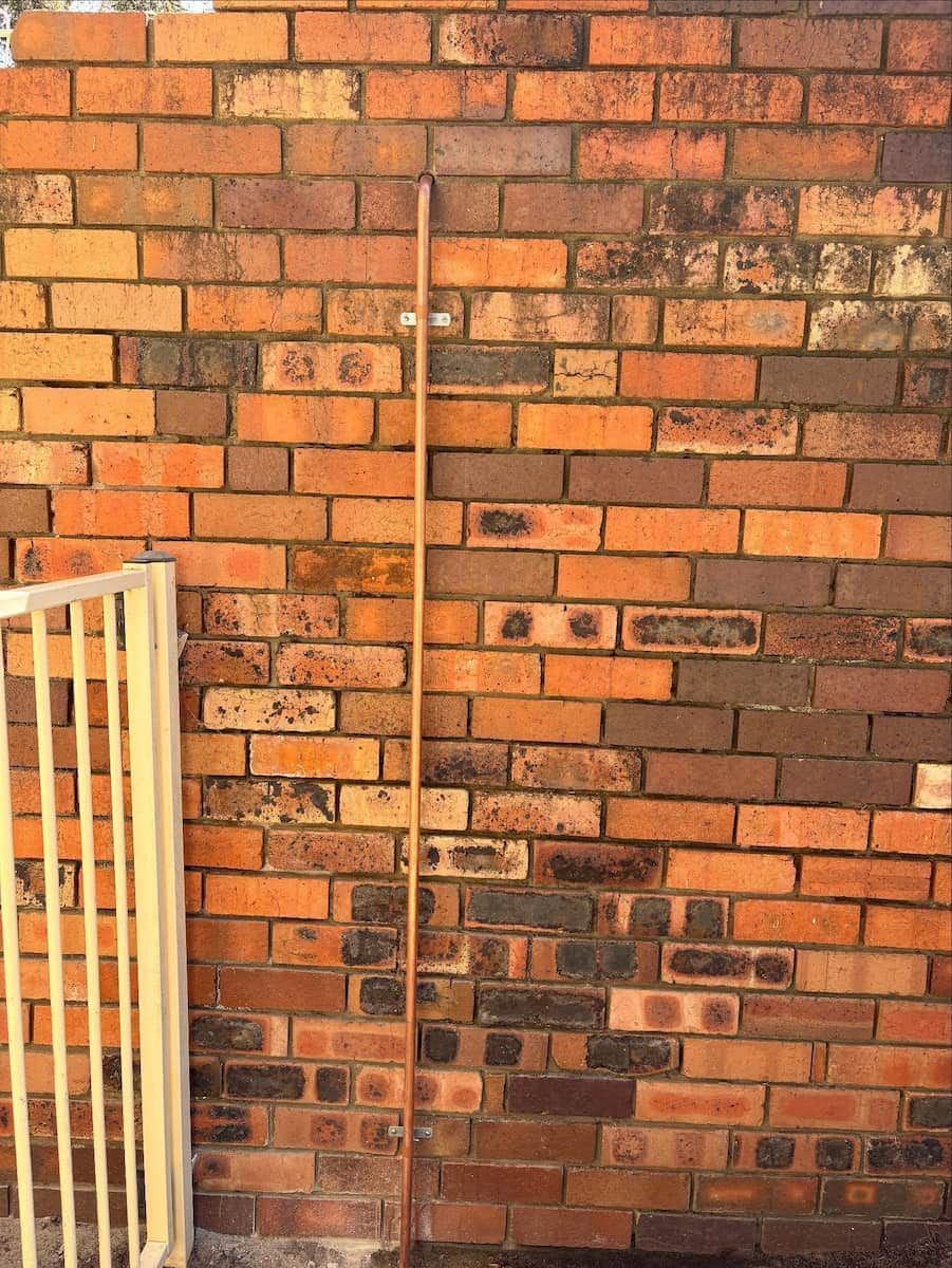 A Vertical Wooden Pole Leaning Against a Textured Brick Wall — Crystal Clear Plumbing & Roofing in Albion Park, NSW