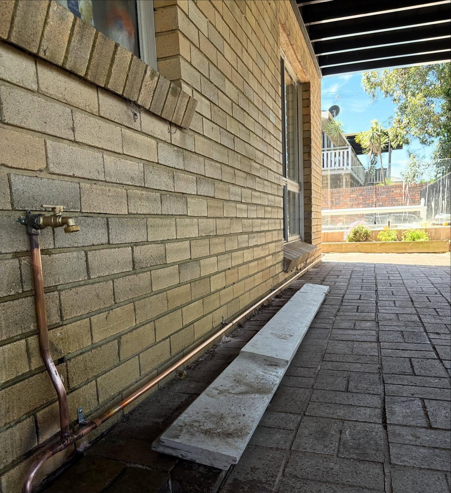 A Copper Pipe and Outdoor Tap on a Tan Brick Wall — Crystal Clear Plumbing & Roofing in Wollongong, NSW