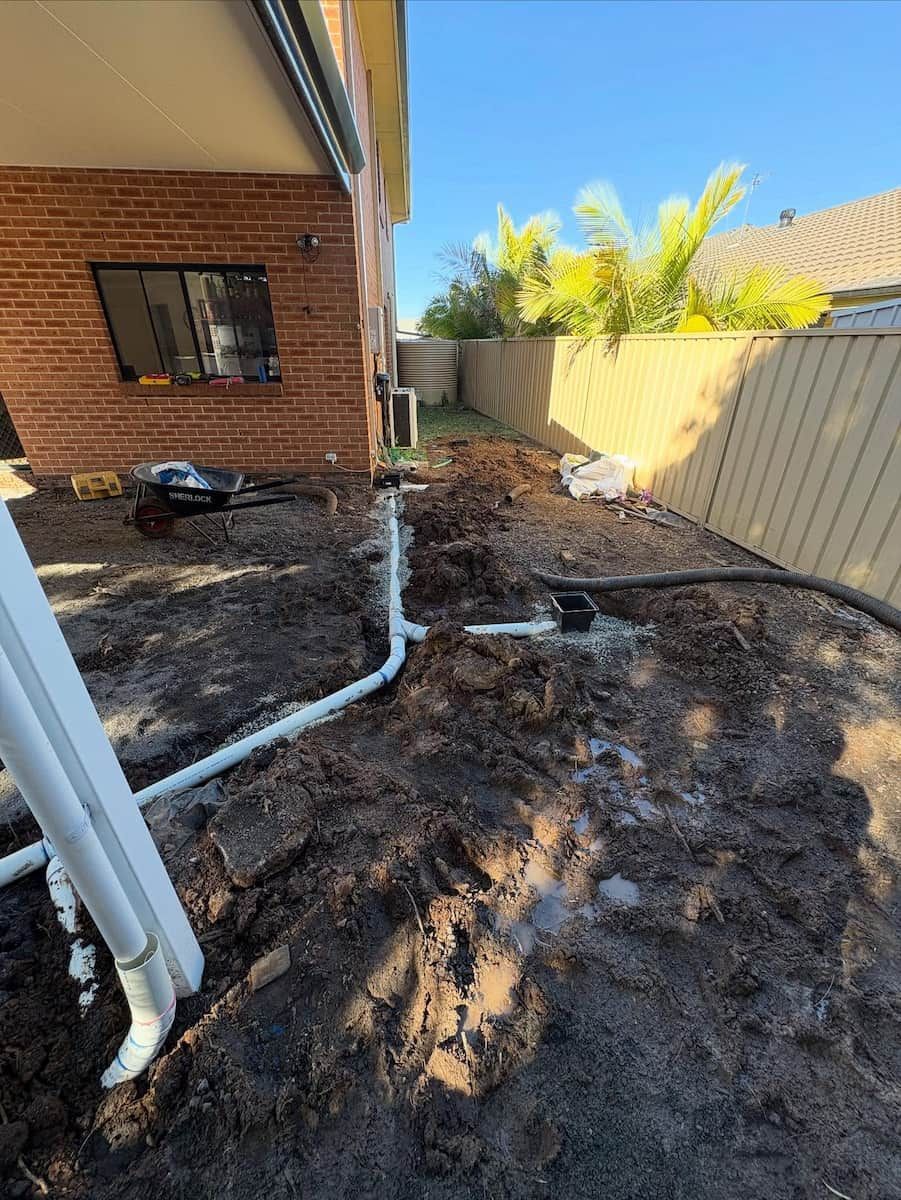 White PVC Plumbing Pipes Installed in a Muddy Trench — Crystal Clear Plumbing & Roofing in Wollongong, NSW
