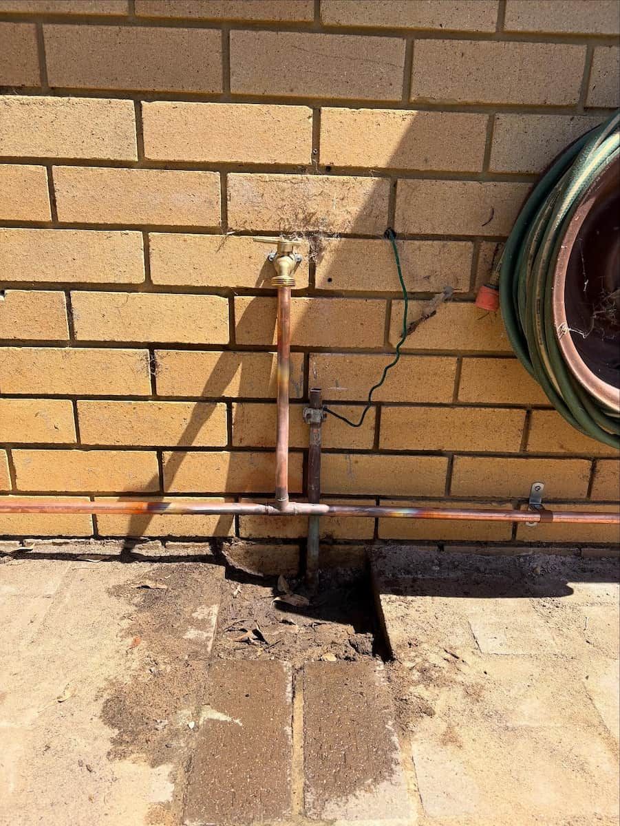 Outdoor Water Tap With Copper Plumbing Pipes Mounted on a Brick Wall — Crystal Clear Plumbing & Roofing in Wollongong, NSW