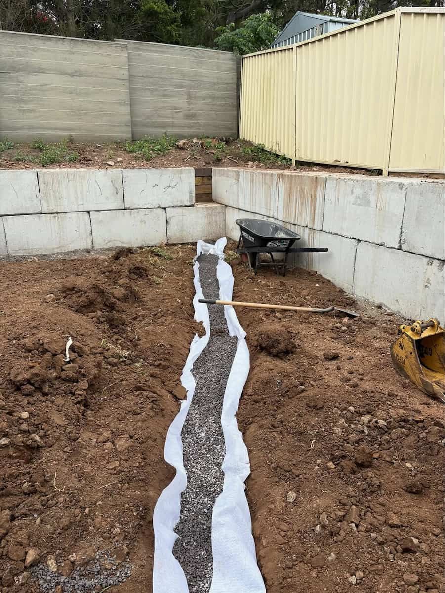 A Trench Lined With White Landscape Fabric and Filled With Dark Gravel — Crystal Clear Plumbing & Roofing in Wollongong, NSW