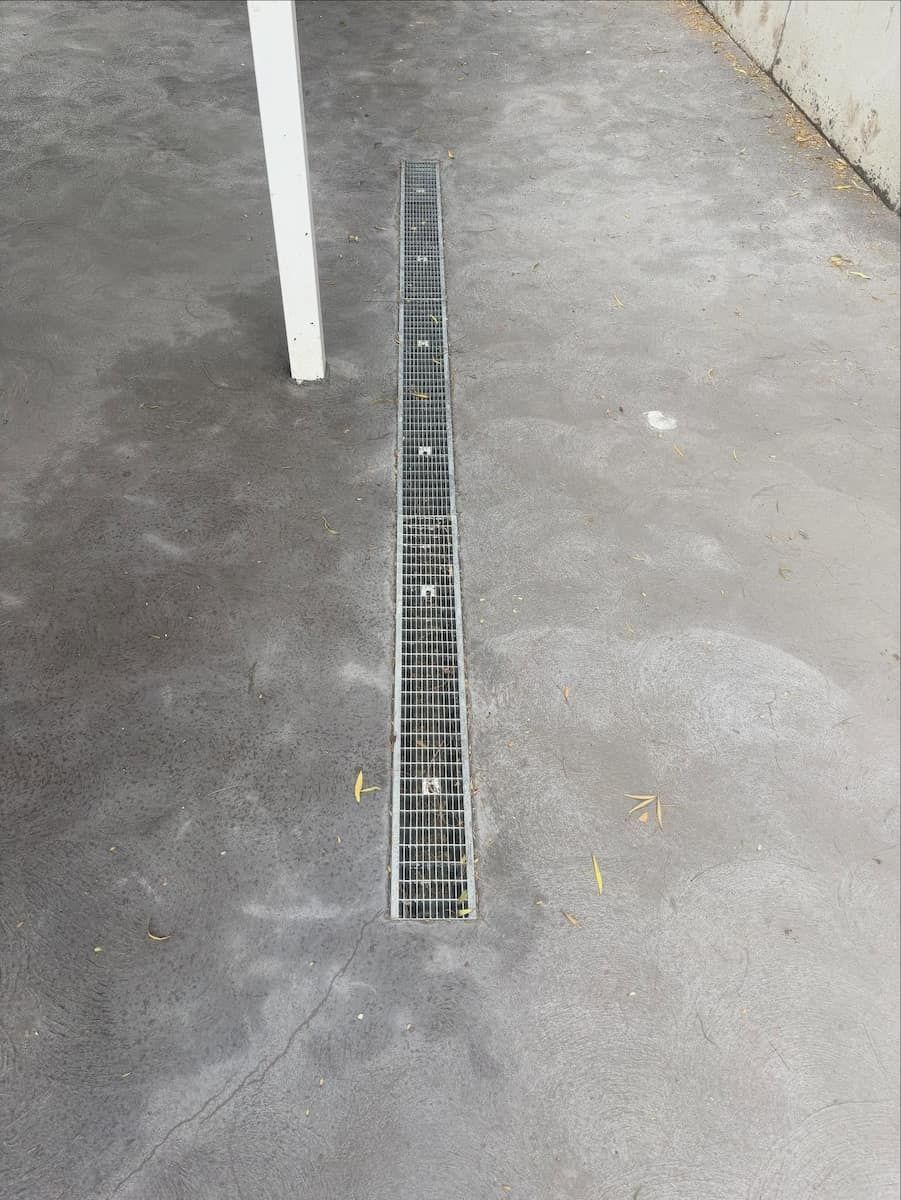 A Metal Drainage Grate Set Into a Concrete Surface Next to a White — Crystal Clear Plumbing & Roofing in Fairy Meadow, NSW