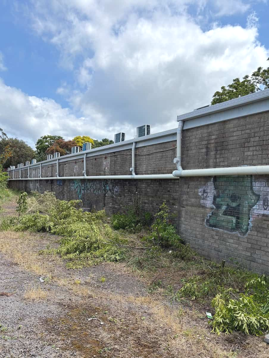 A Long Stone Wall With White Pipes Running Along the Top — Crystal Clear Plumbing & Roofing in Wollongong, NSW