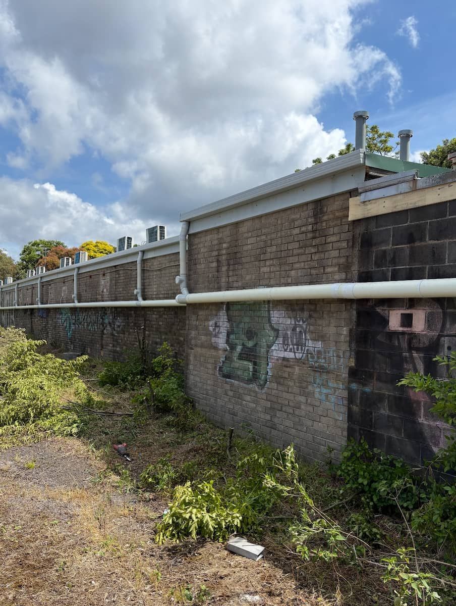 An Outdoor Brick Wall With a White Pipe Running Horizontally  — Crystal Clear Plumbing & Roofing in Shellharbour, NSW