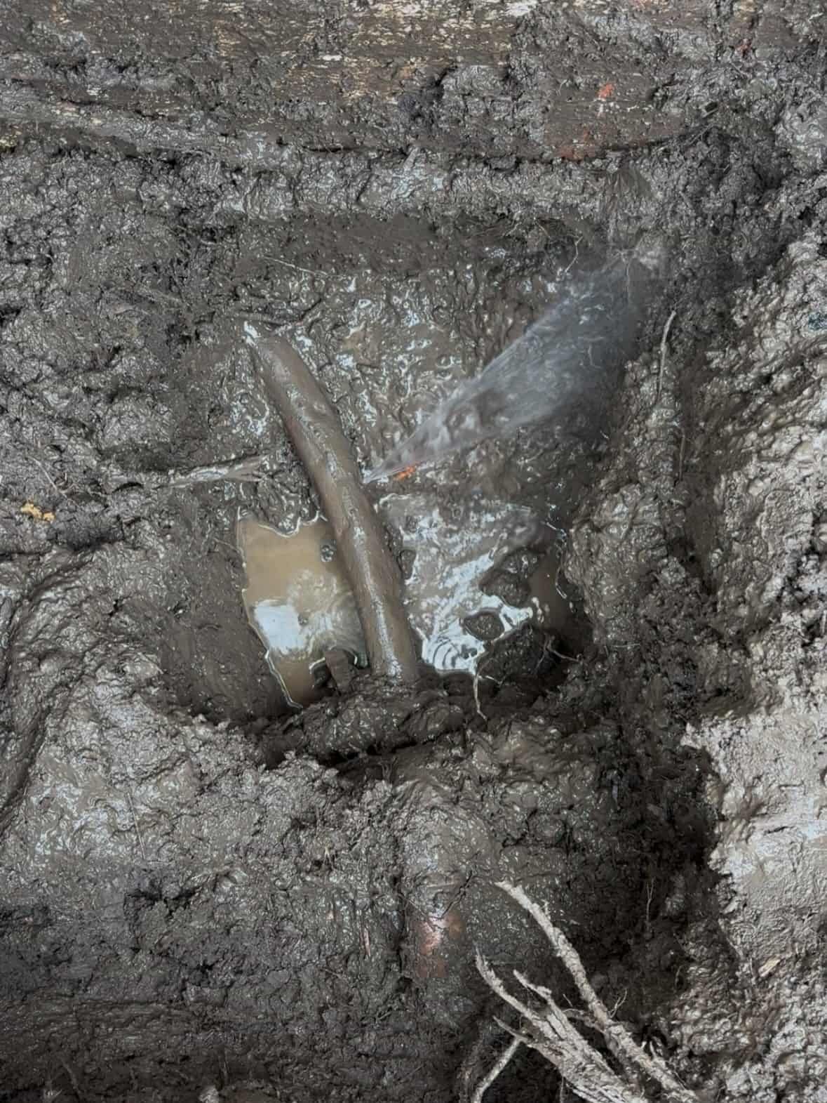 A Leaking Pipe Exposed in a Muddy, Water-filled Trench — Crystal Clear Plumbing & Roofing in Austinmer, NSW