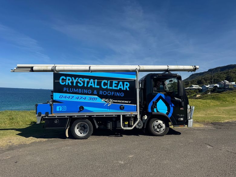 Blue Crystal Clear plumbing truck parked by the ocean under a clear sky — Crystal Clear Plumbing & Roofing in Wollongong, NSW