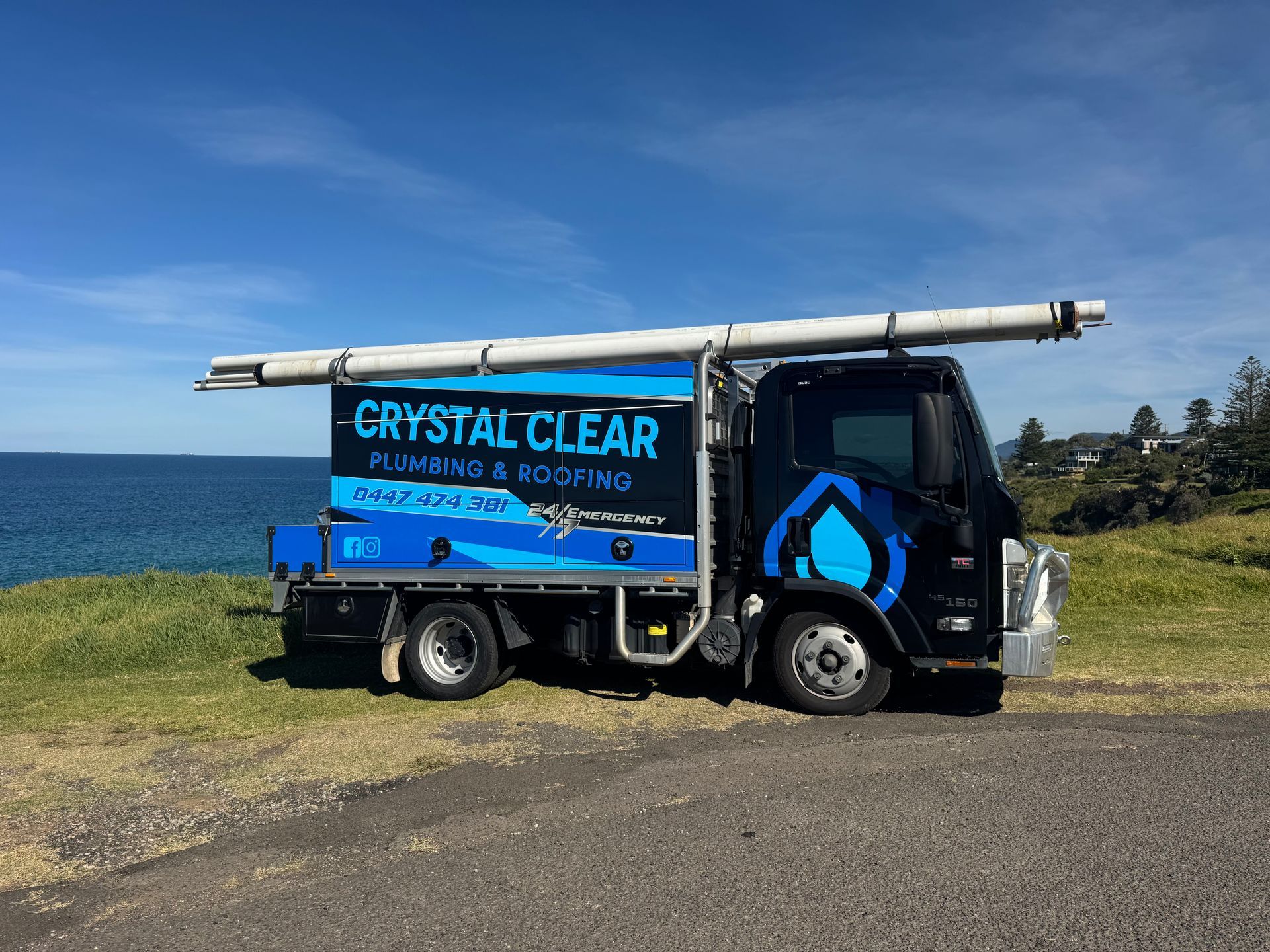 Blue Crystal Clear water truck parked on a grassy coast with ocean and blue sky in the background — Crystal Clear Plumbing & Roofing in Wollongong, NSW