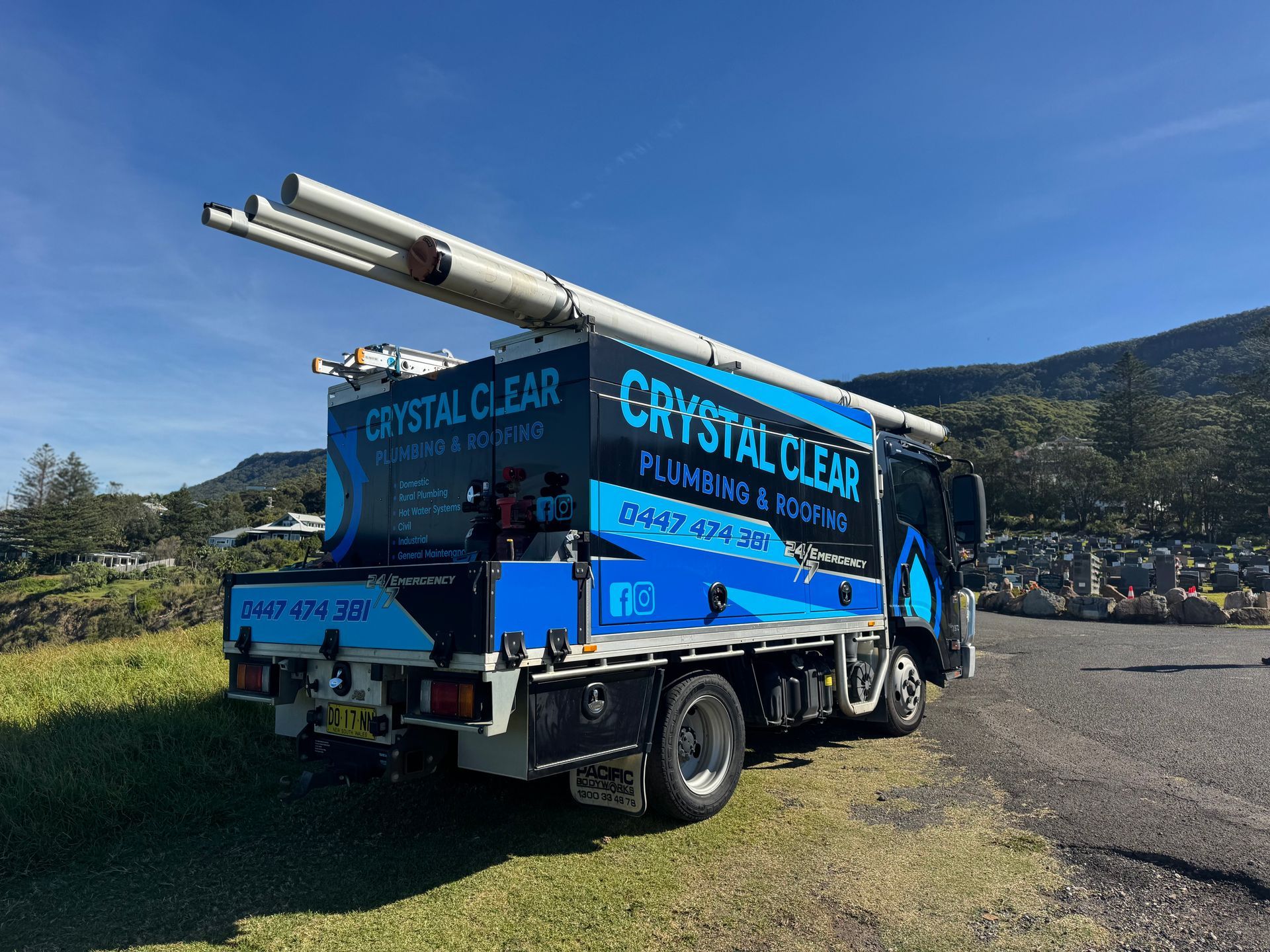 Blue Crystal Clear plumbing truck parked on grass beside mountains under a clear sky — Crystal Clear Plumbing & Roofing in Wollongong, NSW