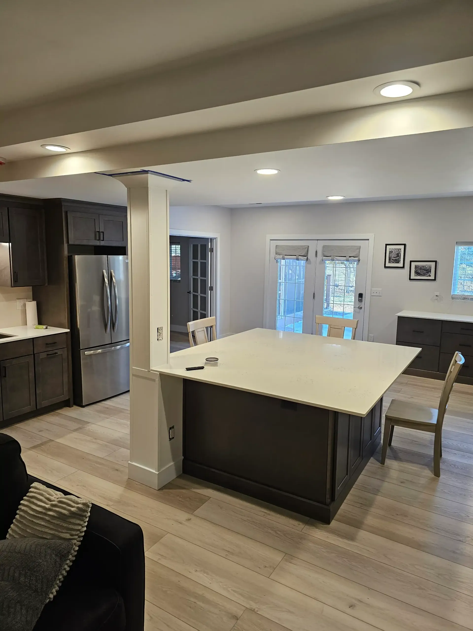 A modern kitchen featuring a dark island with a large white countertop, wood-look flooring, and stainless steel appliances.