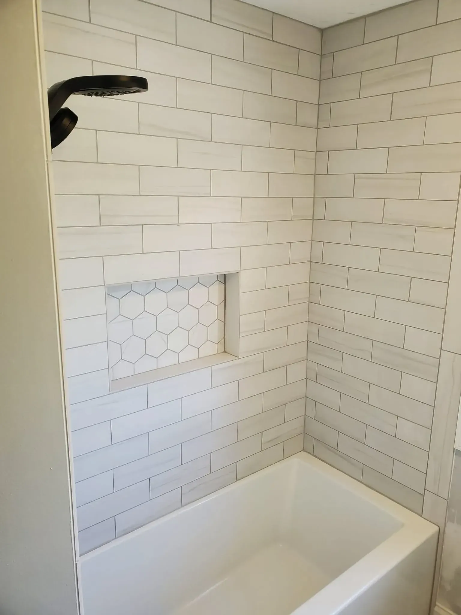 A white tiled shower alcove featuring a black shower head and a decorative hexagon-tiled recessed wall niche.