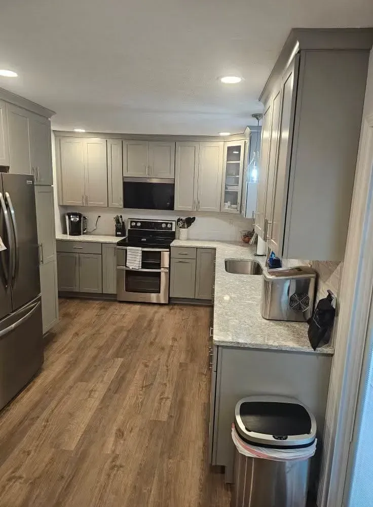 A modern kitchen with grey cabinets, stainless steel appliances, speckled countertops, and wood-look flooring.