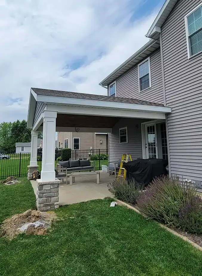 A house with light gray vinyl siding features a covered back patio with stone-based white columns and a concrete floor.