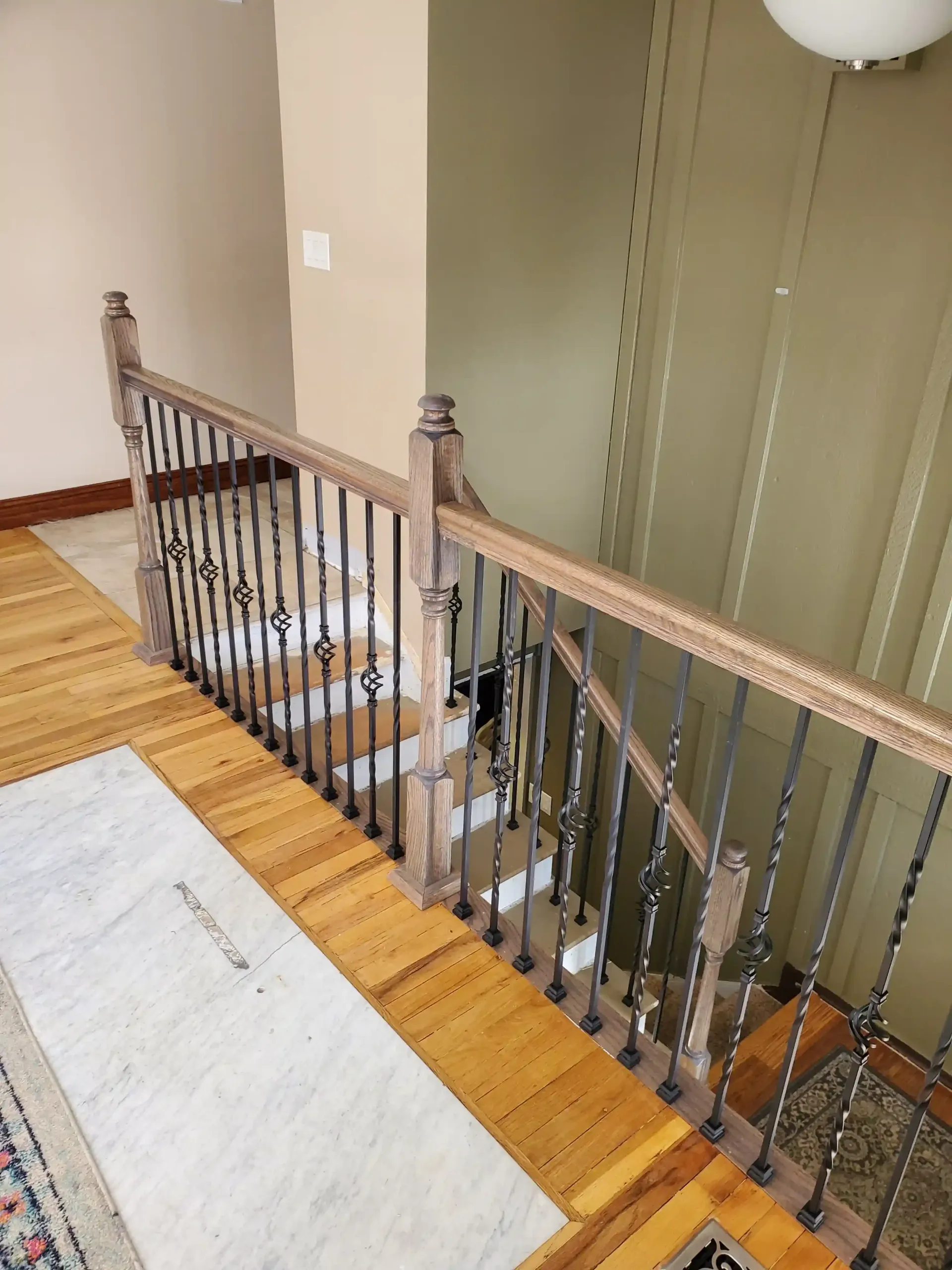 A wooden staircase railing with decorative black iron balusters overlooking a staircase in a home.
