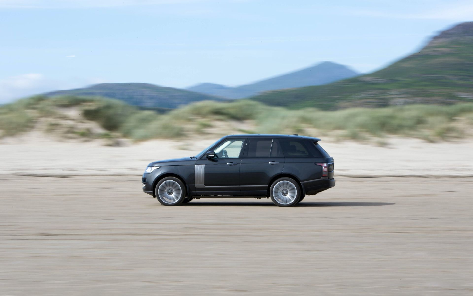 a black range rover is driving on a sandy beach .