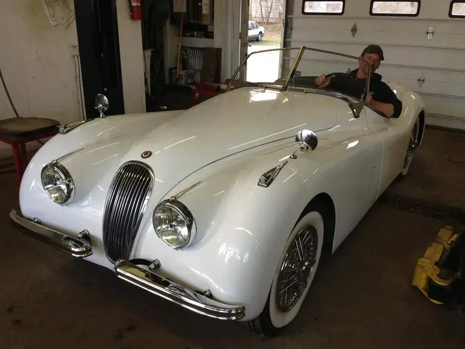 A man is sitting in a white sports car in a garage