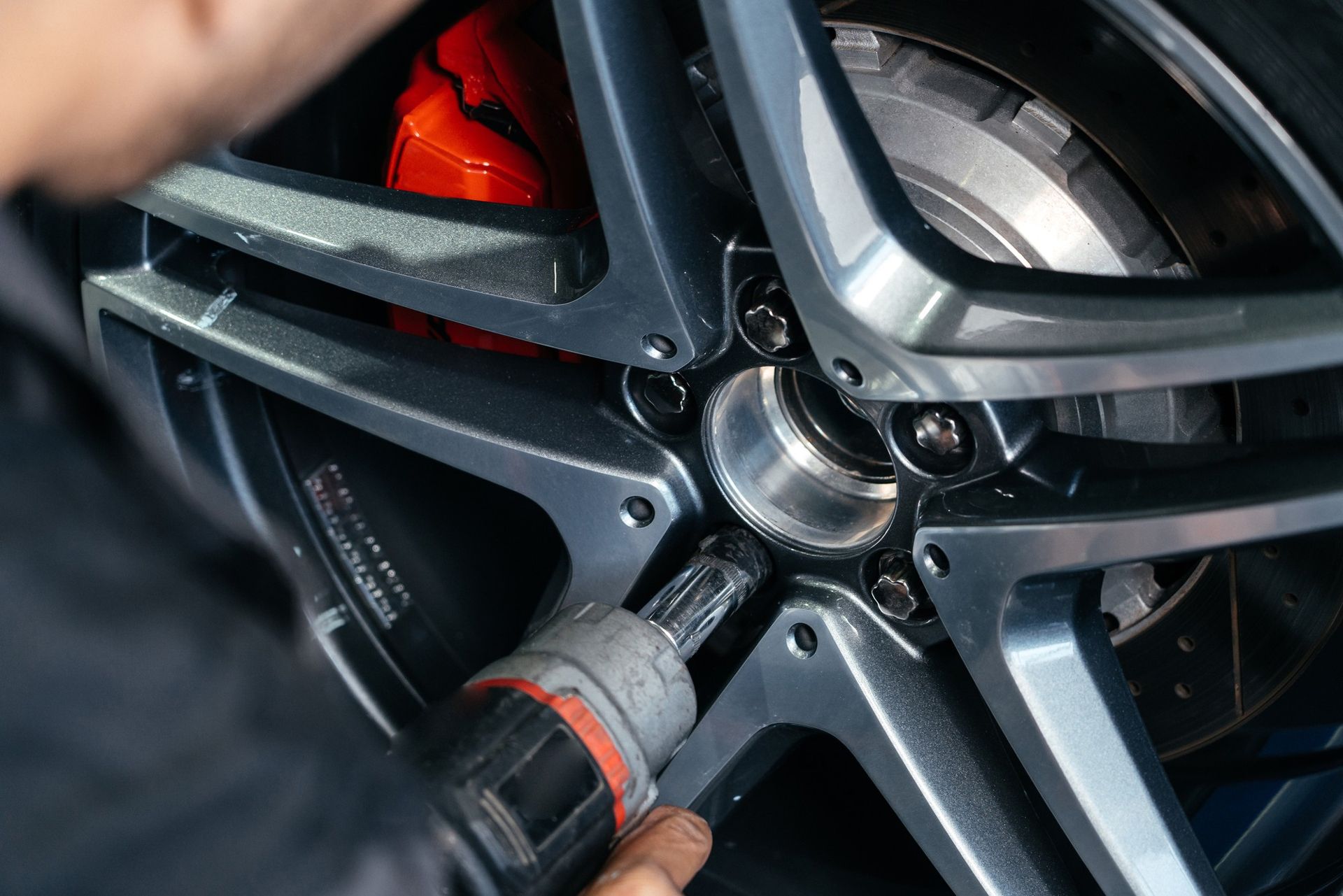 A person is working on a car wheel with a drill.