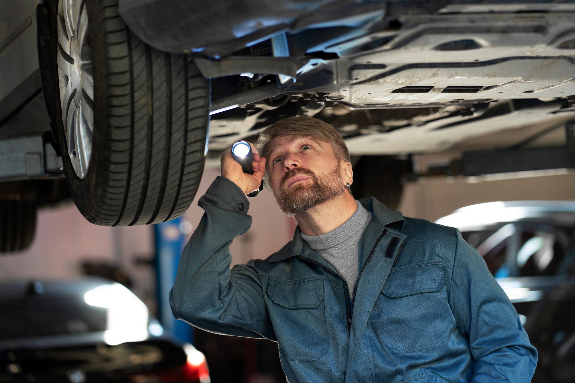 A man is looking under a car with a flashlight.