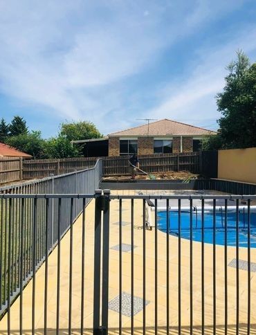A fence surrounds a swimming pool with a house in the background.