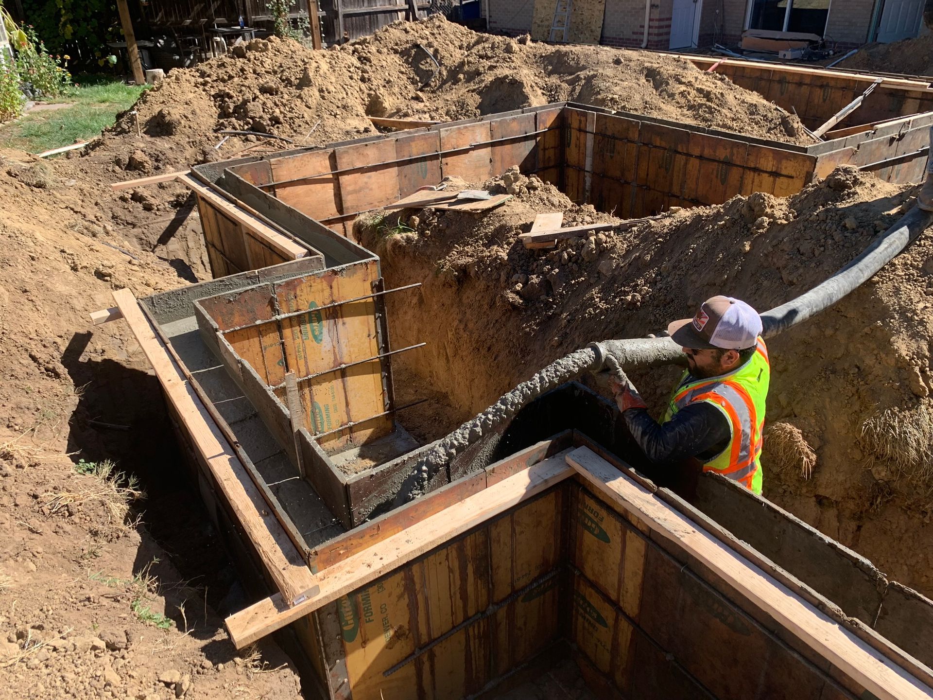 Construction worker pumping concrete into a wooden foundation pit at a building site