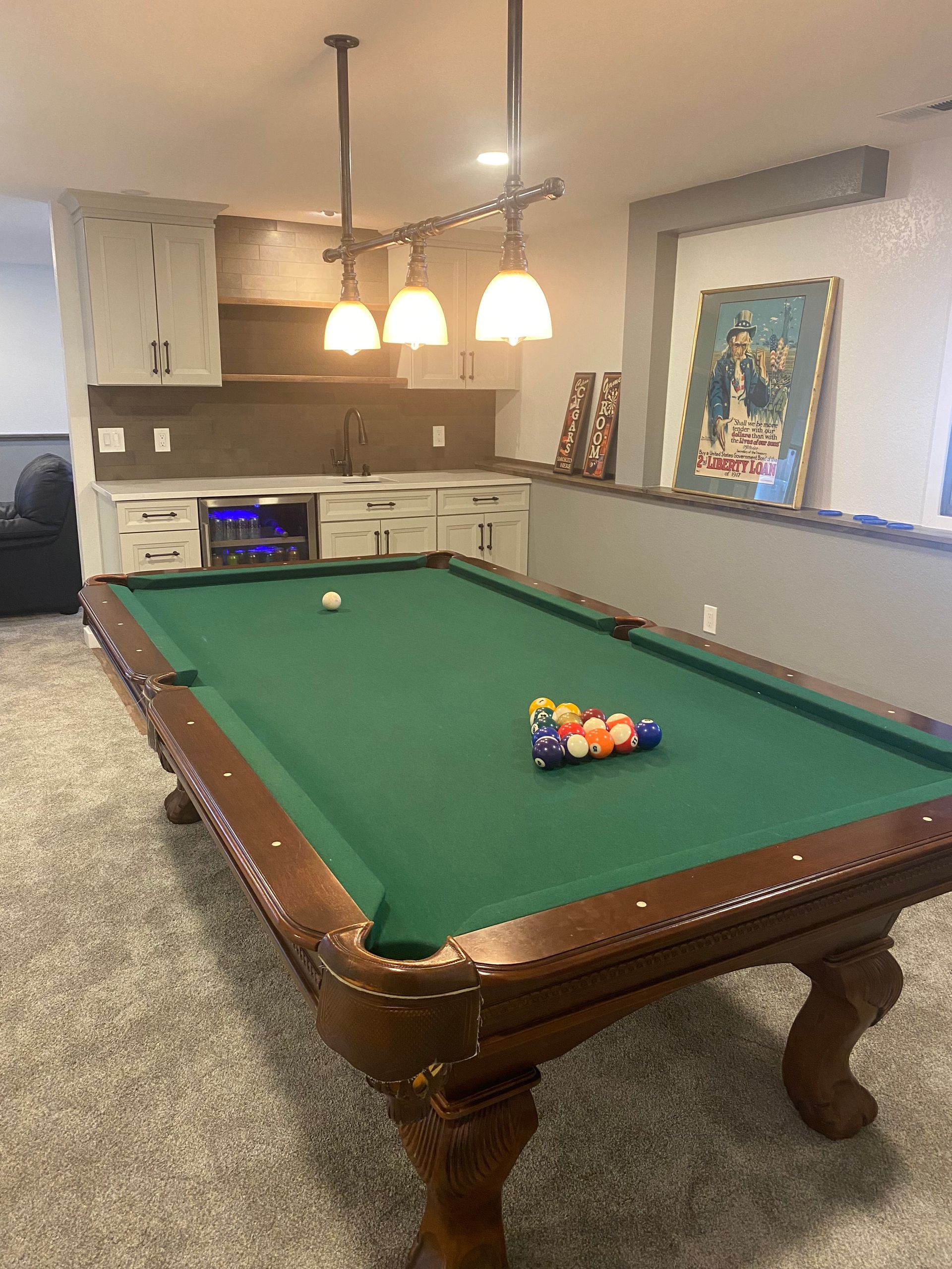 Basement game room with a pool table, hanging lights, and a small TV in the background.