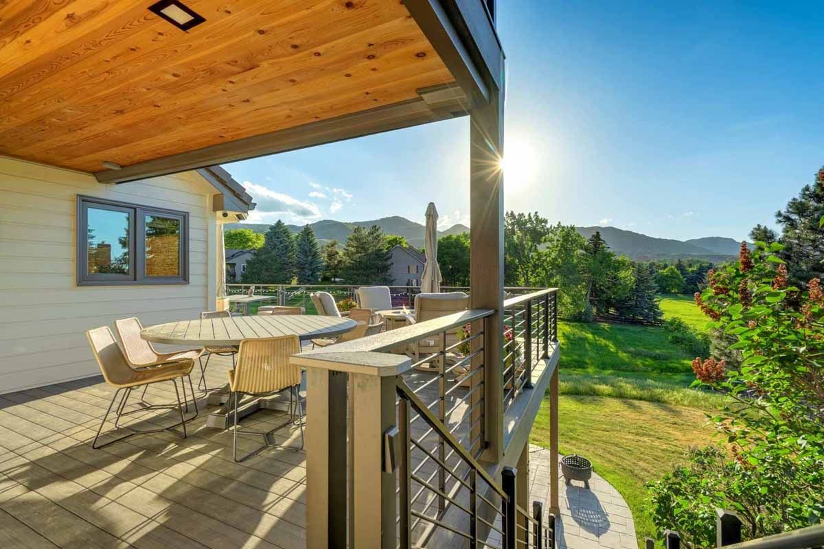 Covered patio with table and chairs overlooking a sunny green yard and hills