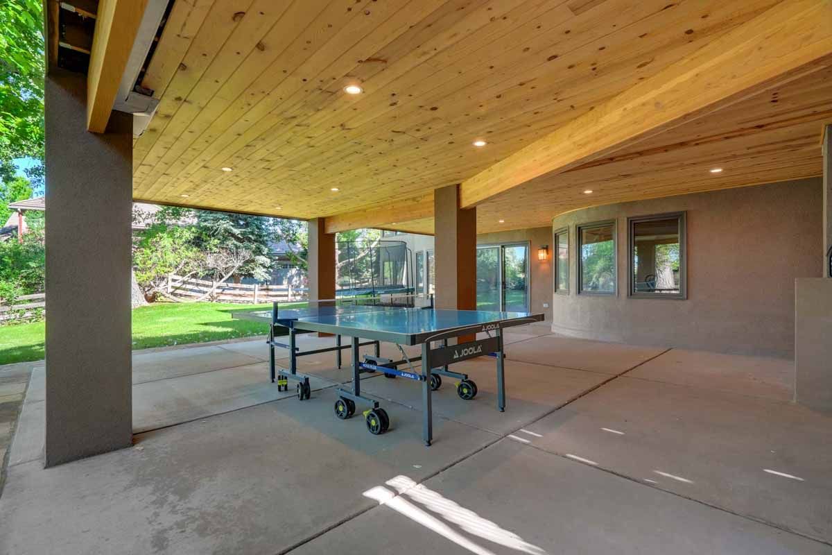Covered patio with ping-pong table, wood ceiling, and concrete floor beside a grassy yard