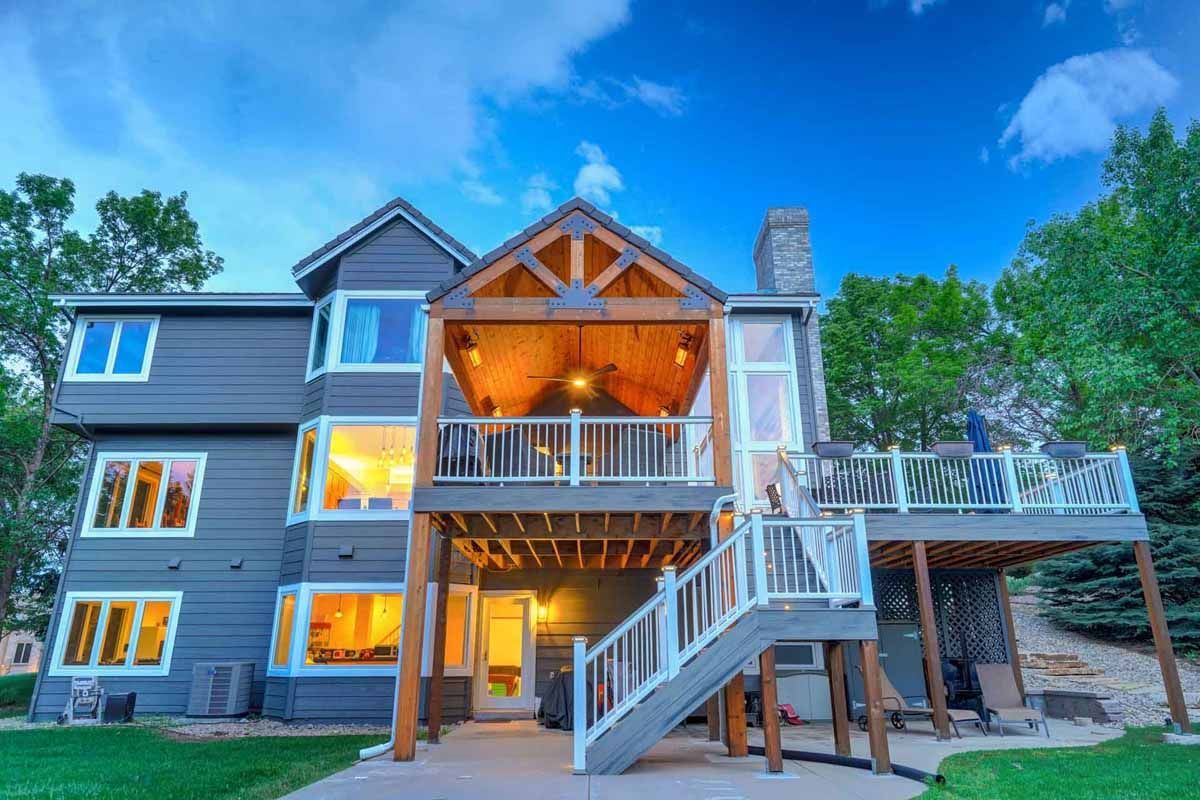 Large rustic house with lit porch and staircase at dusk, surrounded by trees