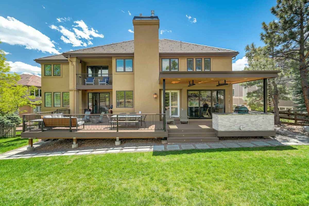 Modern two-story house with a covered patio and large green lawn under a blue sky