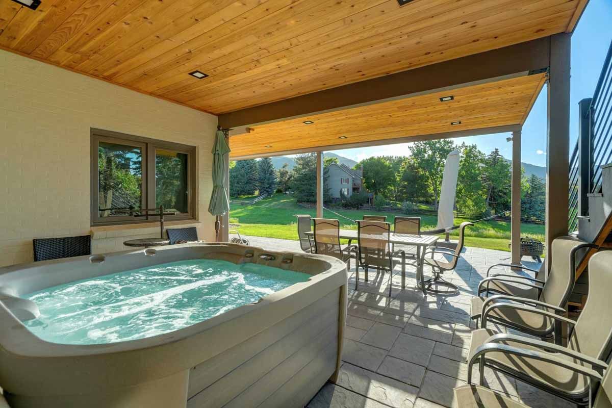 Covered patio with a hot tub, patio chairs, and a view of a green backyard