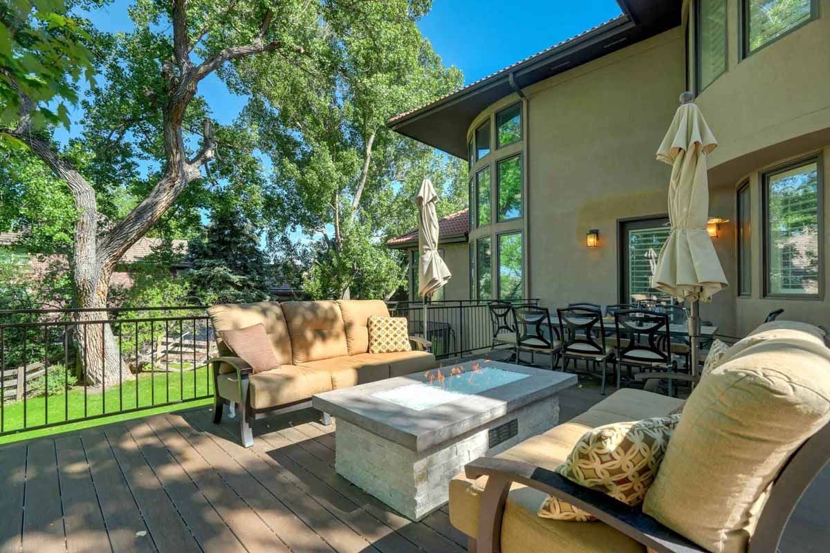 Patio seating area with outdoor sofa, chairs, fire pit, and trees beside a house