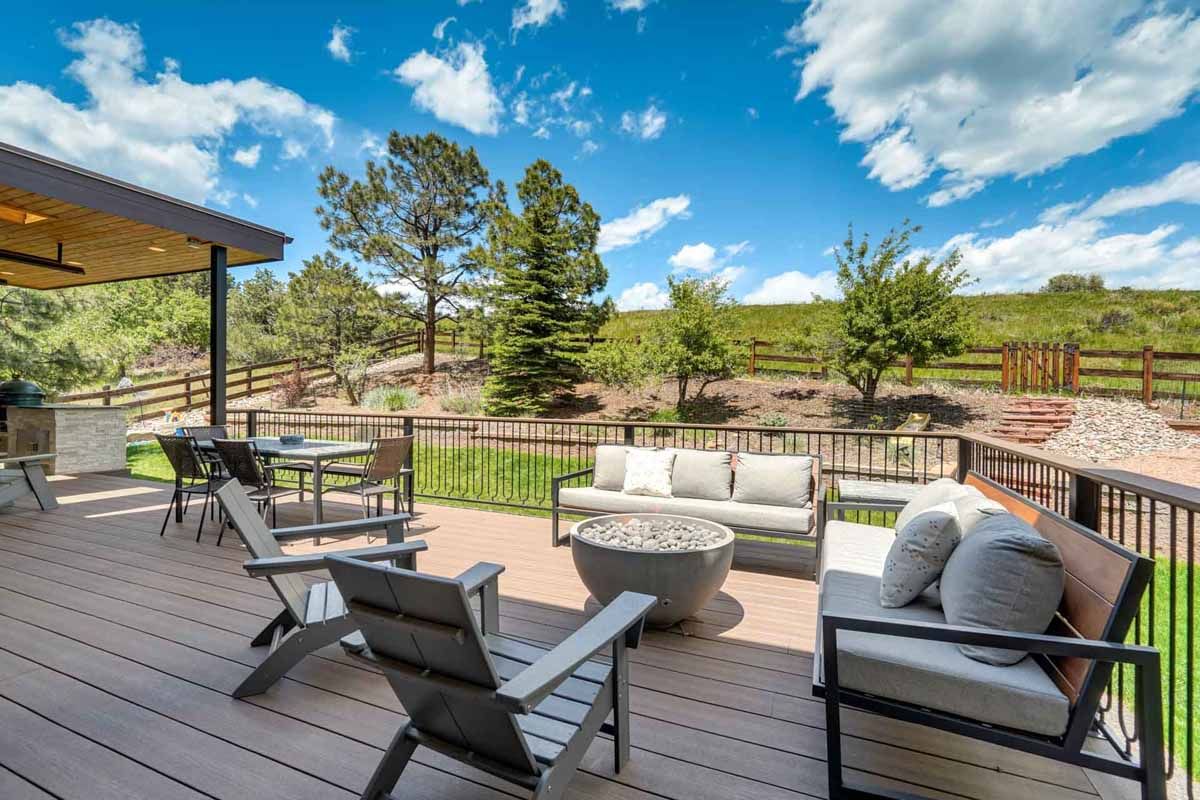 Patio deck with outdoor seating, fire pit, and scenic view of trees and open fields under a blue sky