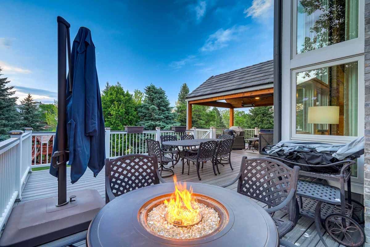 Patio with fire pit, dining table, and covered umbrella on a deck at dusk