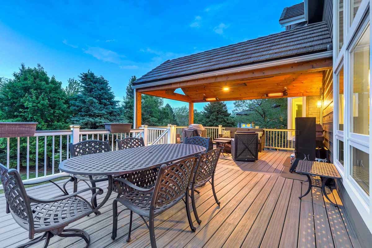 Wooden deck with patio table, chairs, and a covered seating area at sunset