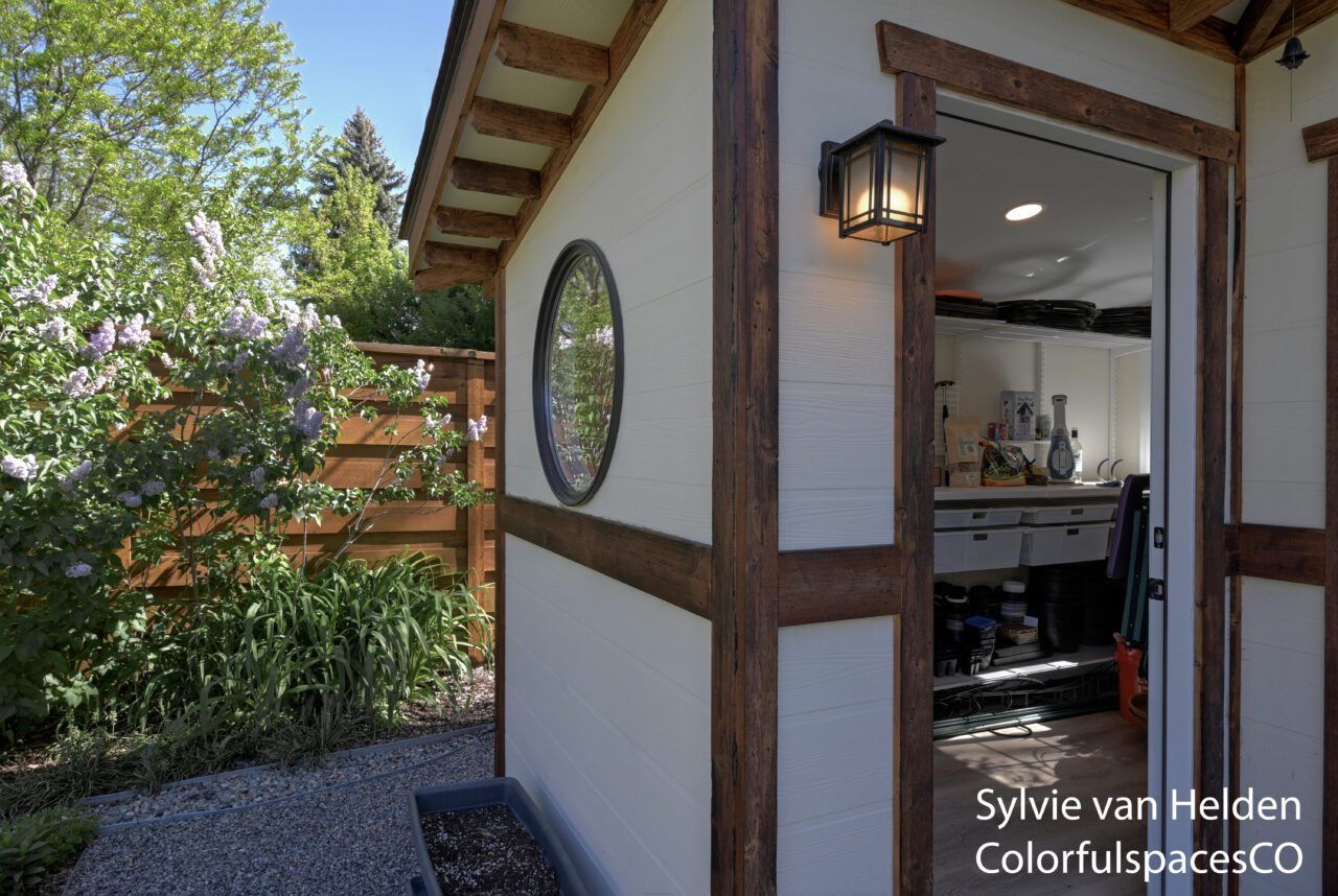 Small cottage doorway with lantern, round window, and open view into a bright interior kitchen.