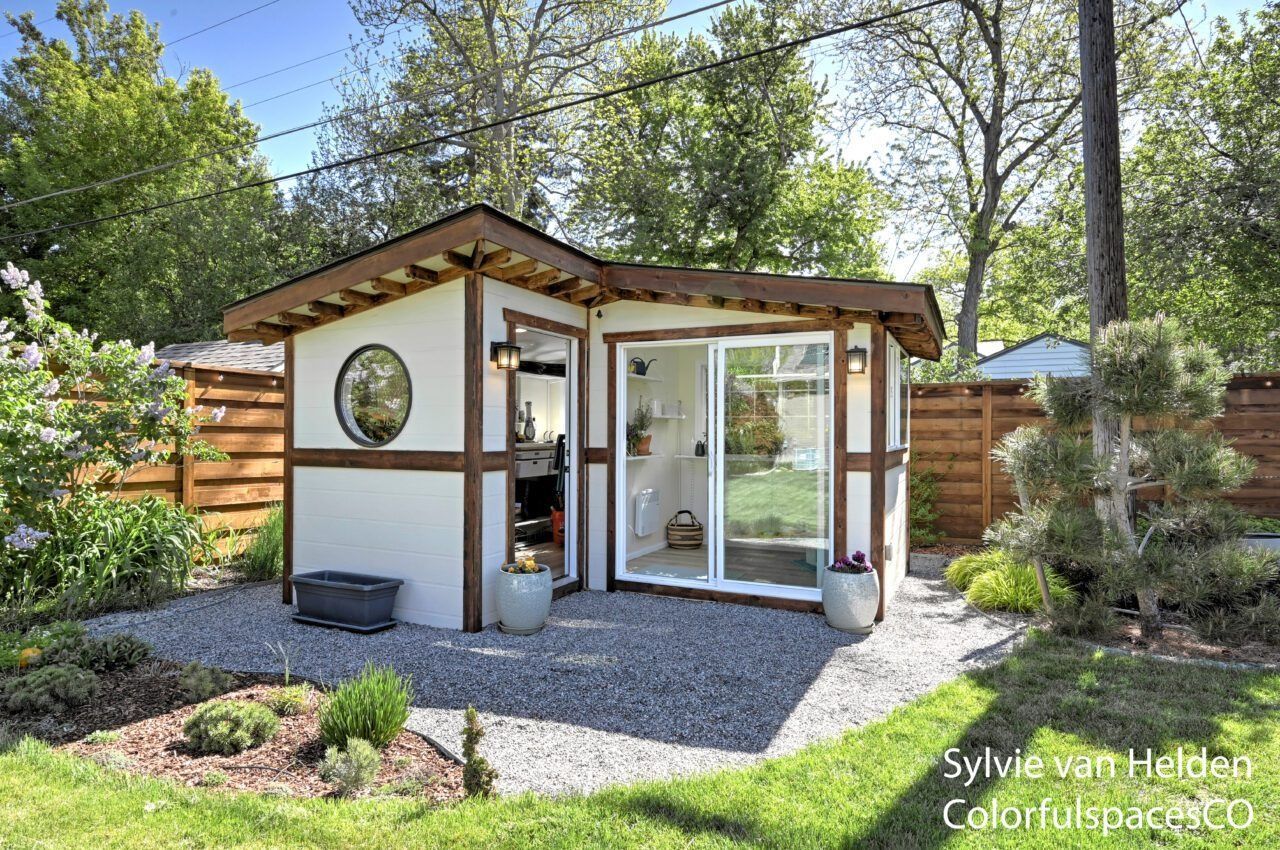 Small modern garden shed with white walls, wood trim, and sliding glass doors in a sunny backyard