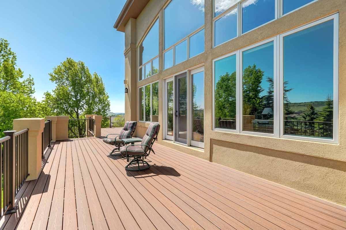 Spacious wooden deck with lounge chairs beside a house with large reflective windows.