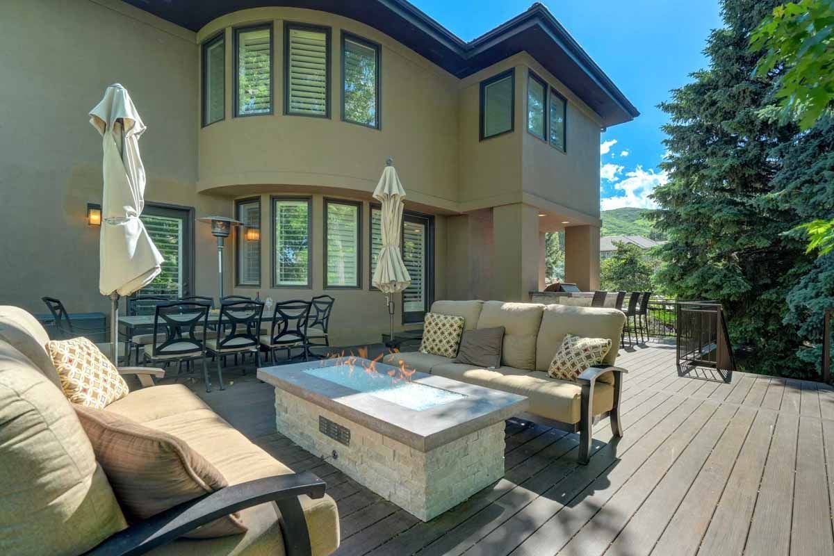 Backyard patio with outdoor seating, fire pit, and umbrellas beside a tan two-story house