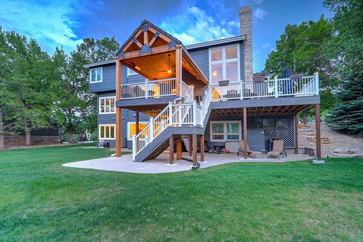 Backyard view of a two-story house with a deck, stairs, and large grassy lawn