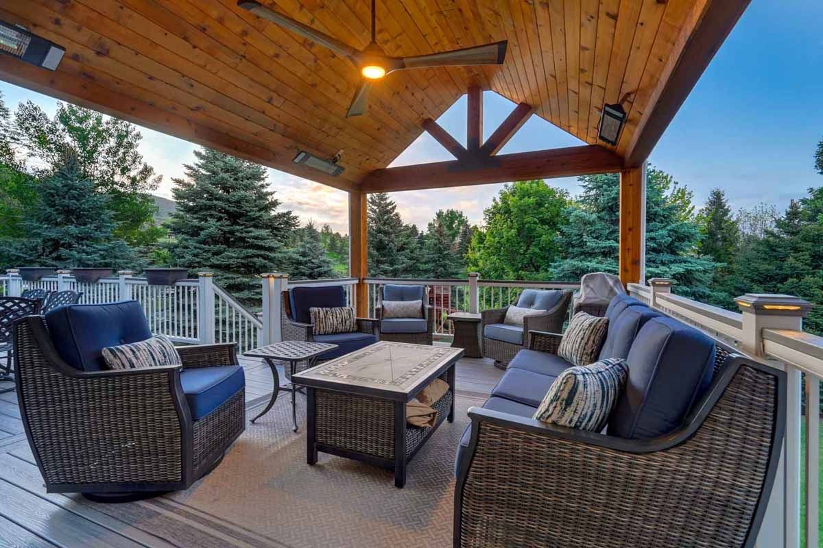 Covered outdoor patio with wicker seating, coffee table, and wooded view at sunset
