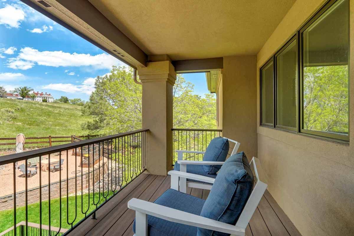 Covered balcony with two blue chairs, railing, and a green hillside view.
