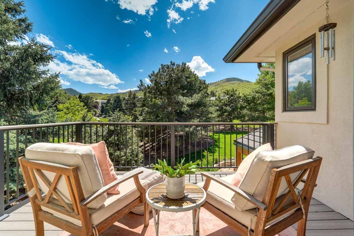 Patio balcony with two cushioned chairs, a small table, and a view of trees under a blue sky