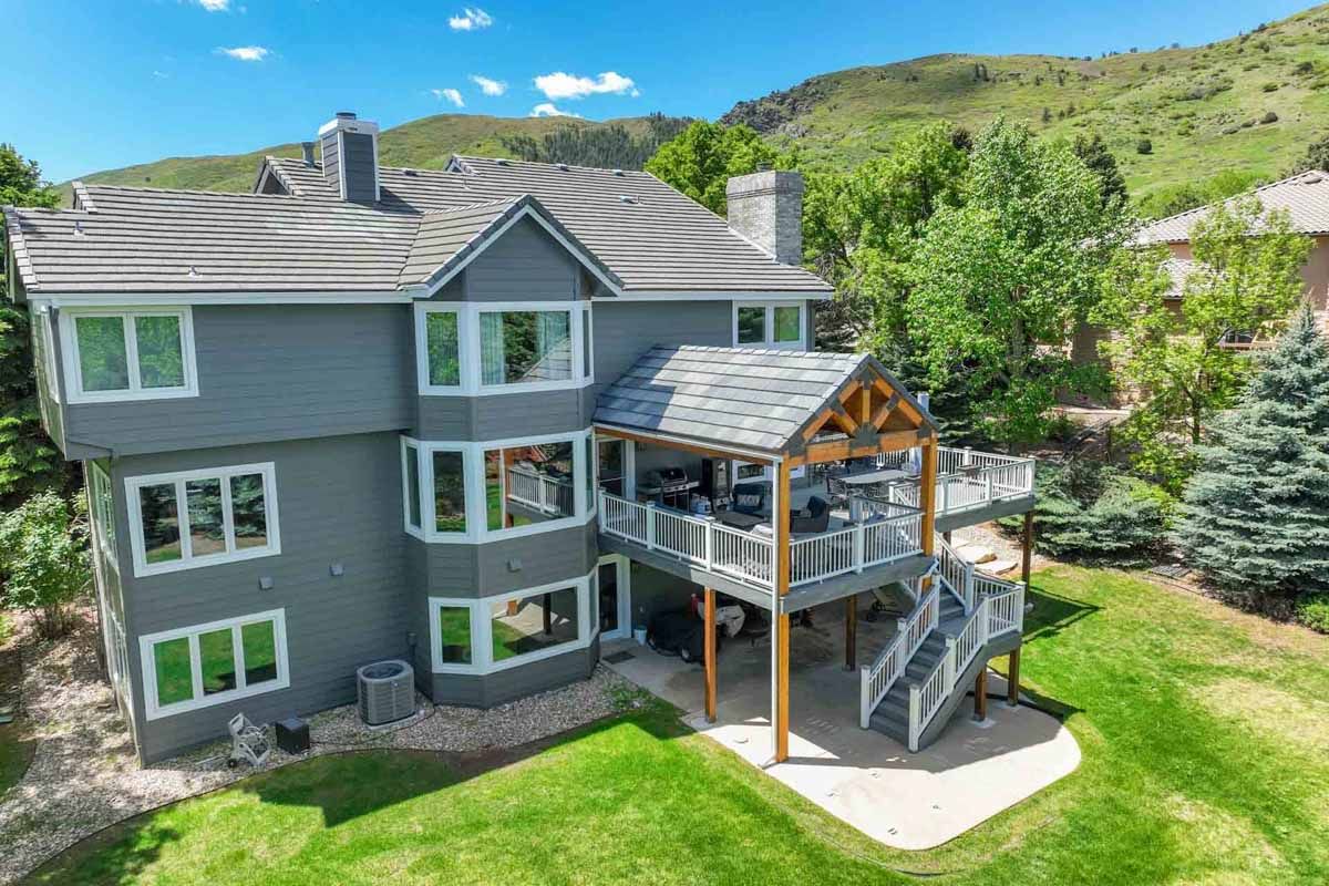 Modern gray multi-story house with a covered deck on a grassy hillside under a sunny sky