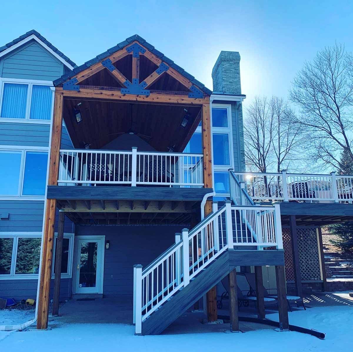 Snow-covered house with wooden balcony, exterior stairs, and a chimney in winter.