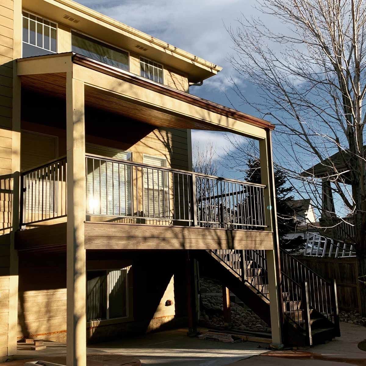 Two-story tan apartment building with balconies and exterior stairway on a sunny day