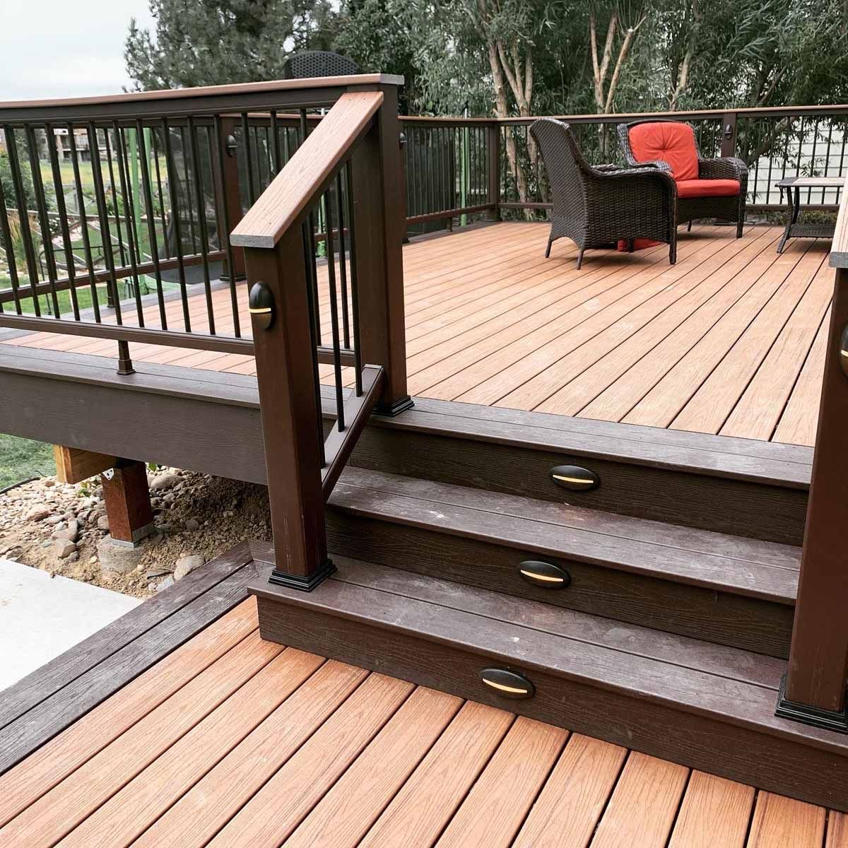 Wooden deck with steps, black railing, and wicker chairs around a small table outdoors