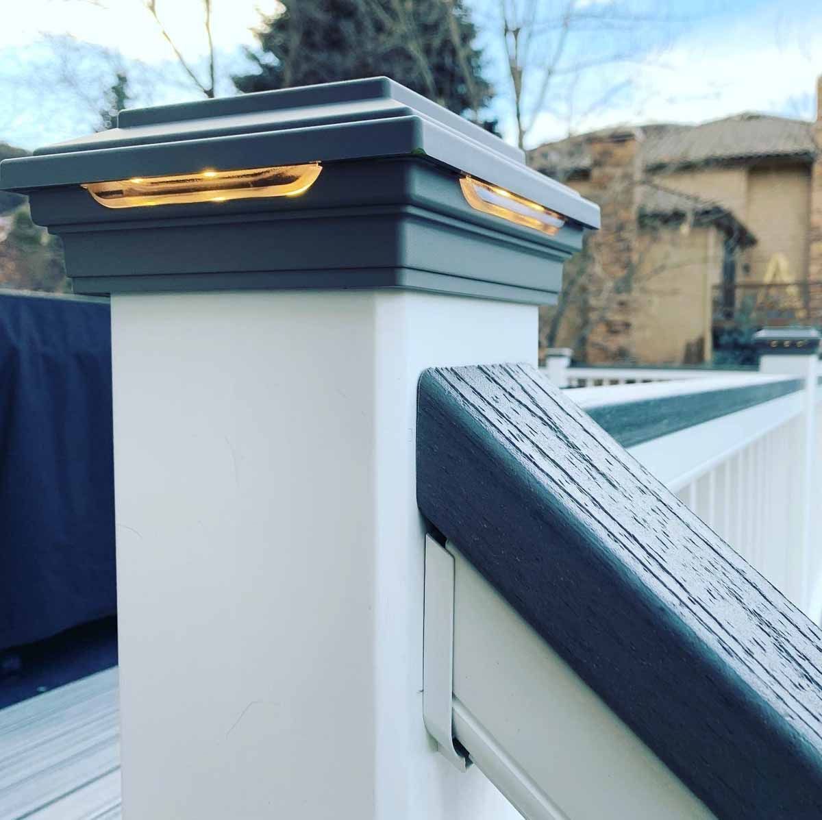 White fence post with dark cap and warm light against a snowy suburban background