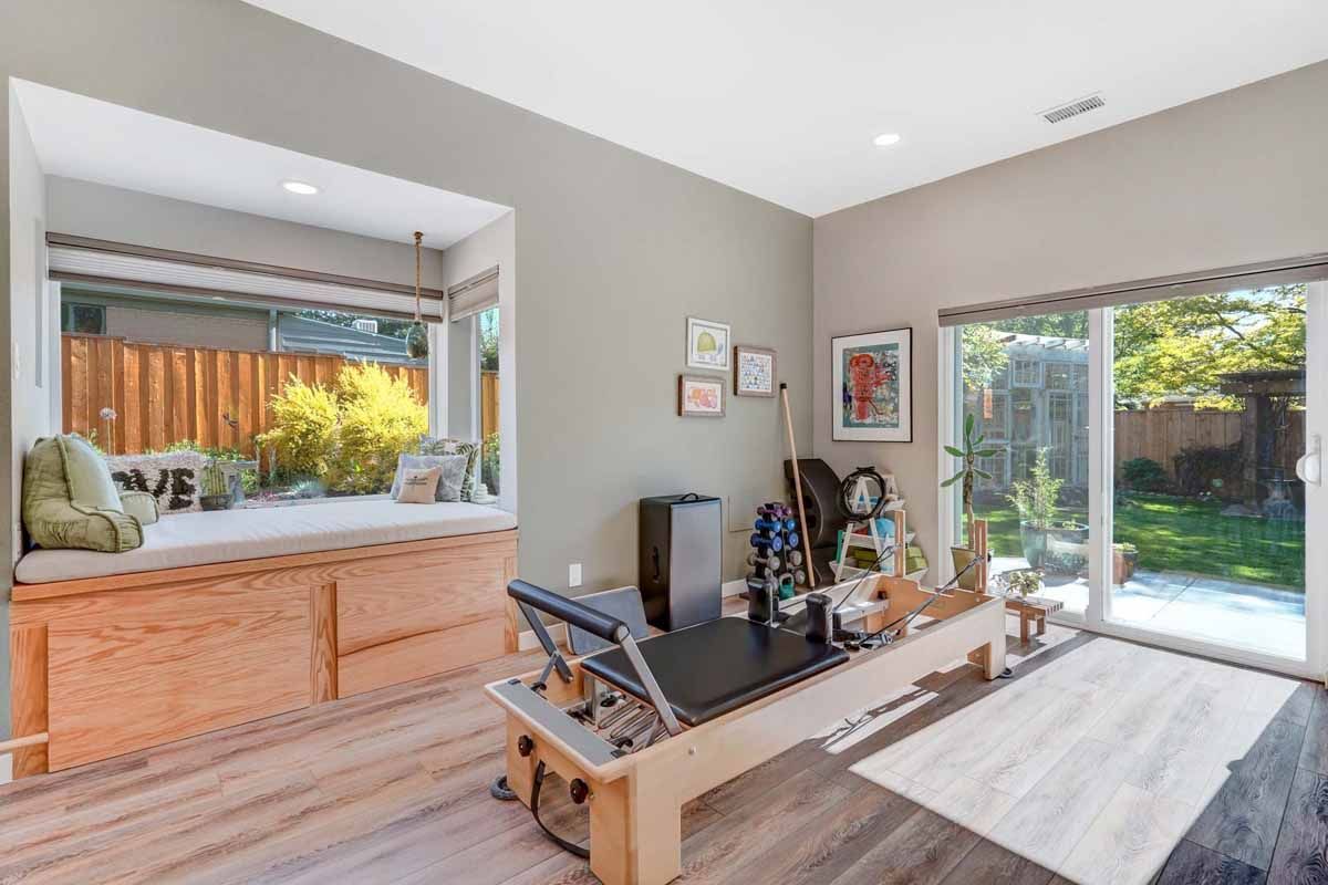 Bright home office with desk, printer, bench seat, and a large window to a sunny patio.