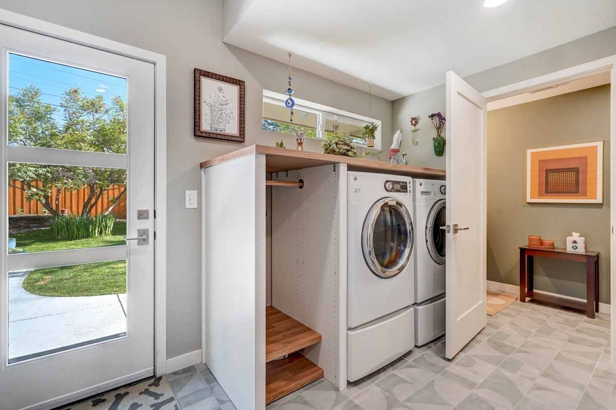 Laundry room with washer and dryer, open storage shelves, and a door to a sunny yard.